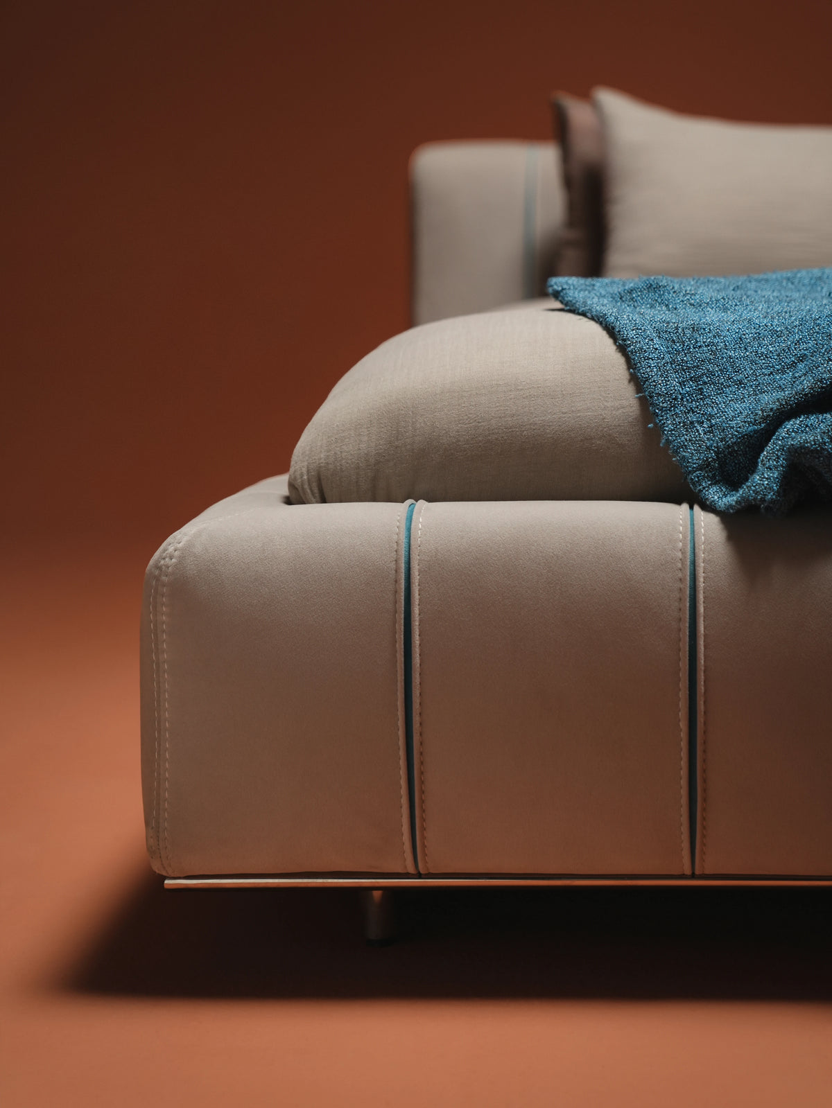 Close view of the Lush bed’s rounded beige upholstered frame, blue seam detailing and slim stainless steel tube base.