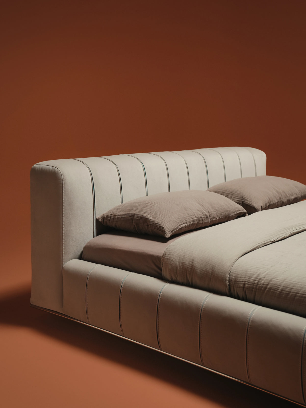 Close angled view of the Lush bed’s rounded upholstered headboard and frame, finished in beige with contrasting blue seam detailing.