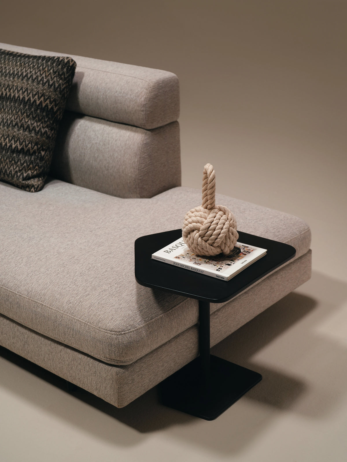 Close-up of the beige Monti sofa with layered backrest heights, a cushioned seat, and a slim black side table.