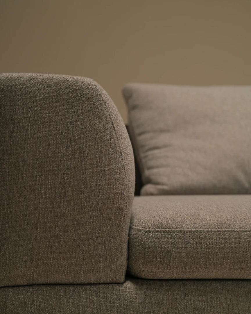 Close-up of the Monti sofa in textured beige upholstery, highlighting its rounded bombé armrest, seat cushion, and soft back cushion.