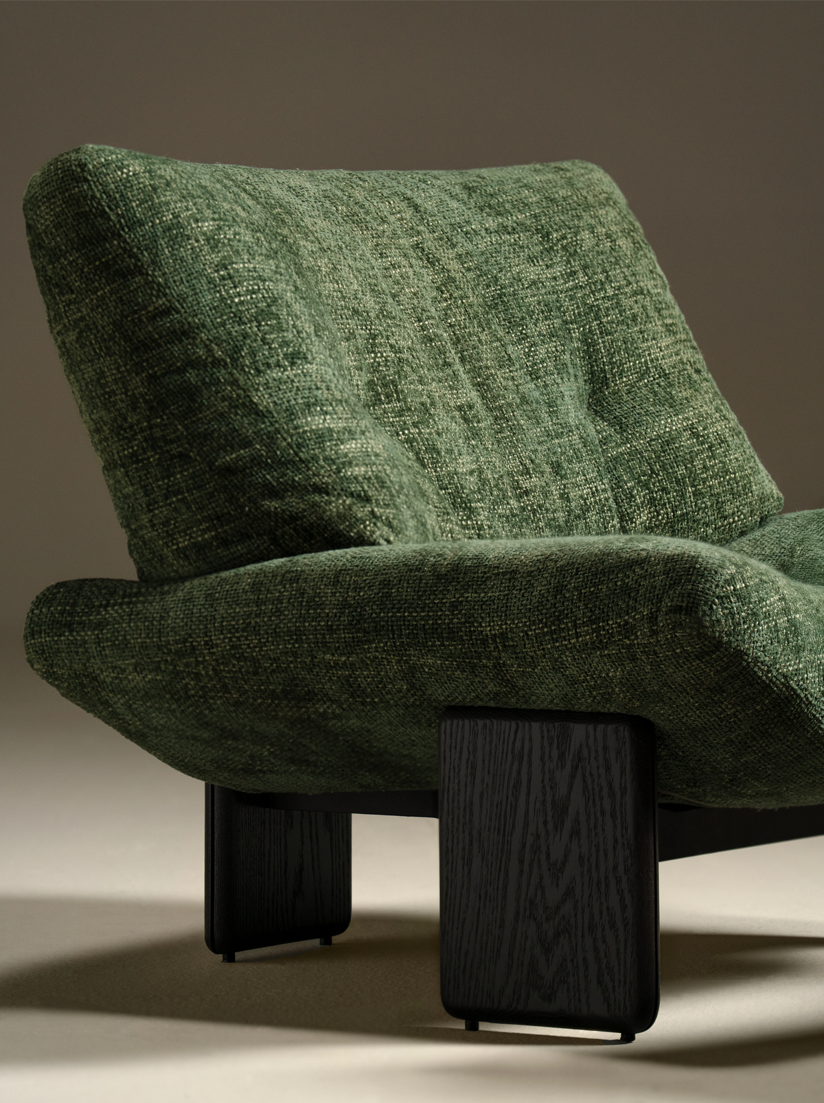 Close view of the green Muse lounge chair showing its gently raised seat sides, capitonné tufting, and dark solid wood slab legs.