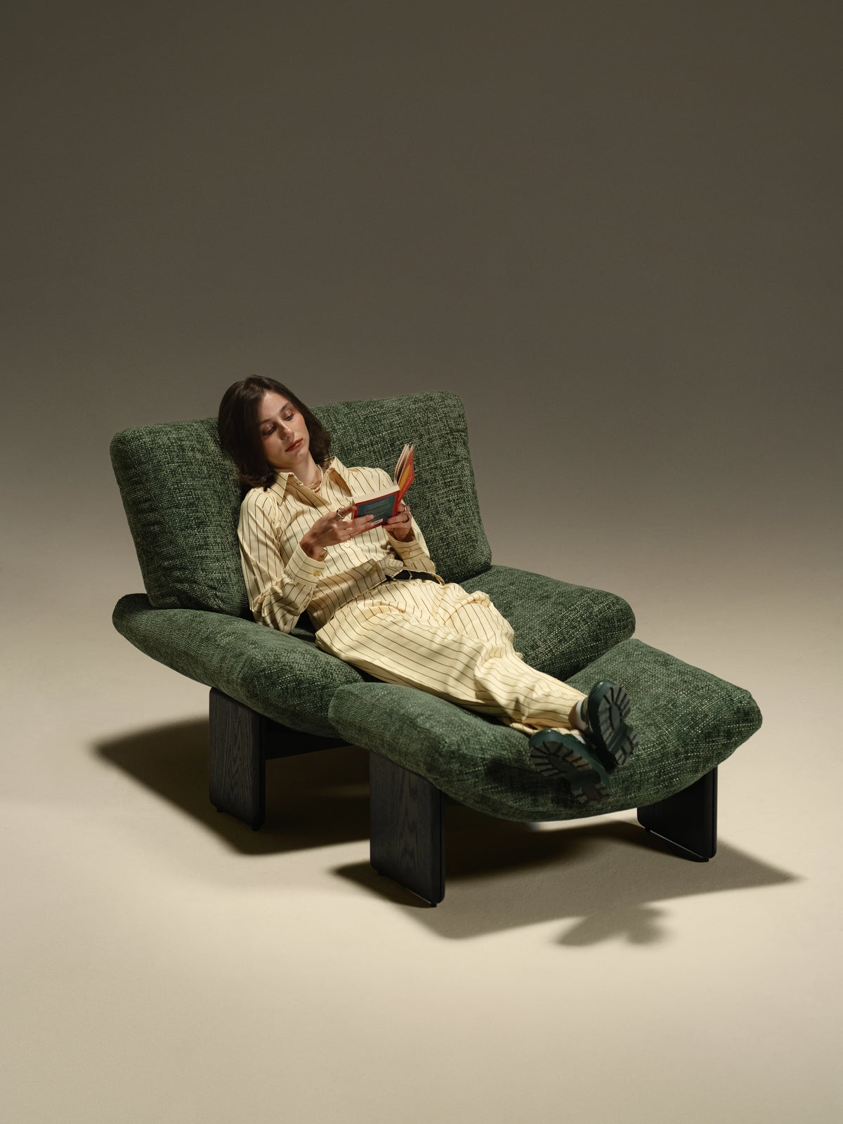 Woman reading in the green Muse lounge chair with her feet resting on the matching upholstered footstool.