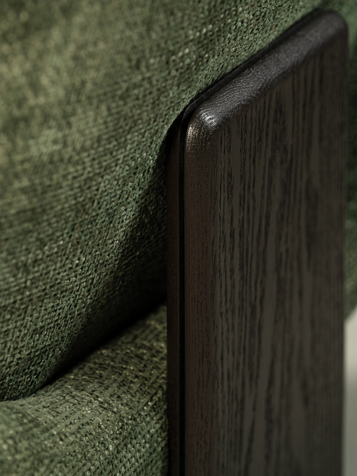 Close-up of the Muse lounge chair showing its green textured upholstery and rectangular dark solid wood slab leg.