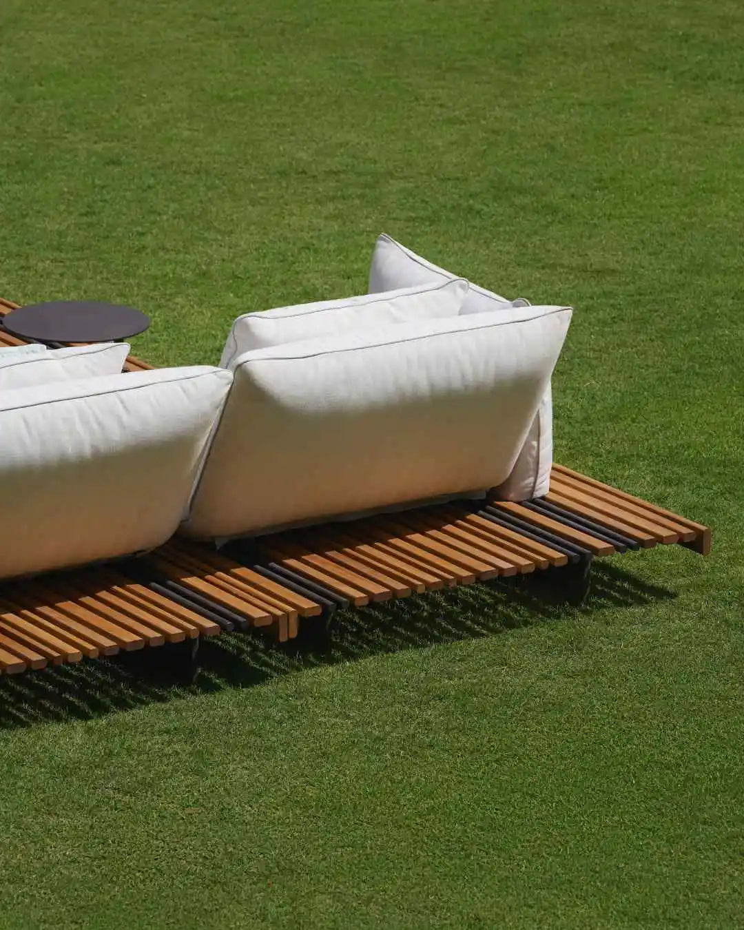 Rear view of the Nest outdoor sofa showing its adjustable backrests and mixed-width teak platform with stainless steel details.