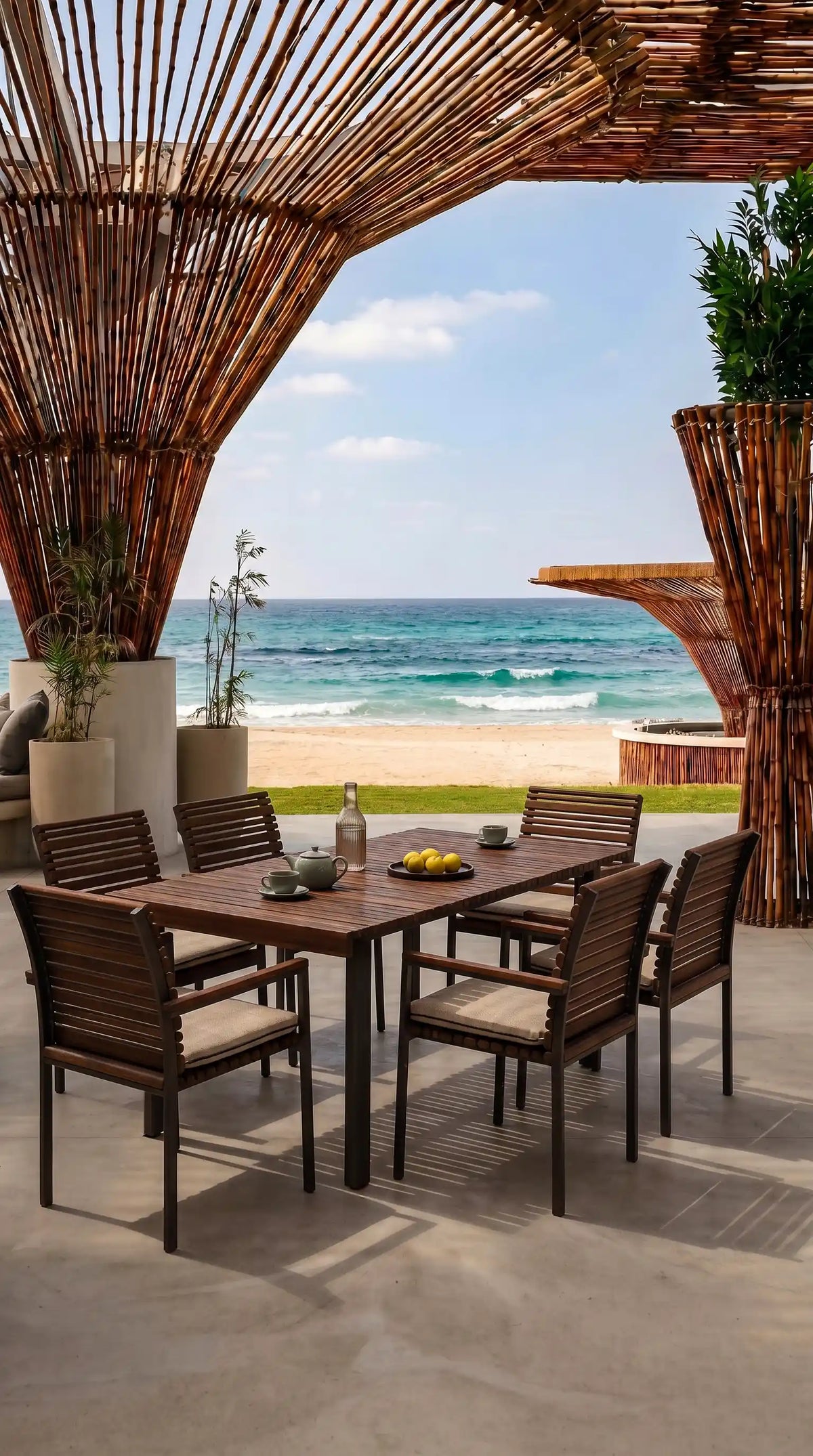 Nest outdoor dining set with a rectangular teak slatted table and six matching cushioned chairs on a beachside terrace.