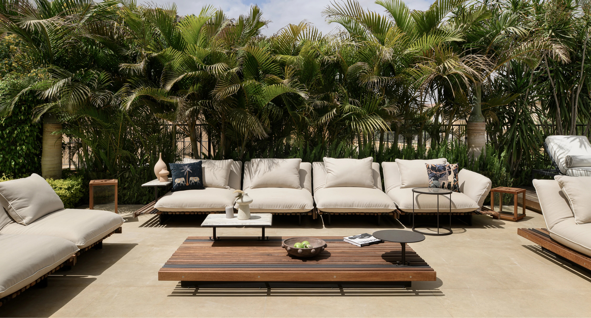 Nest modular outdoor sofa and chaise longue arranged around a slatted teak table in a landscaped garden.