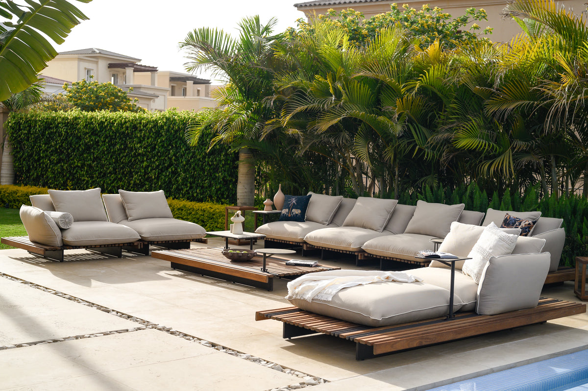 Nest outdoor sofa and chaise longue with white piped cushions, teak platforms, and a matching table on a garden patio.