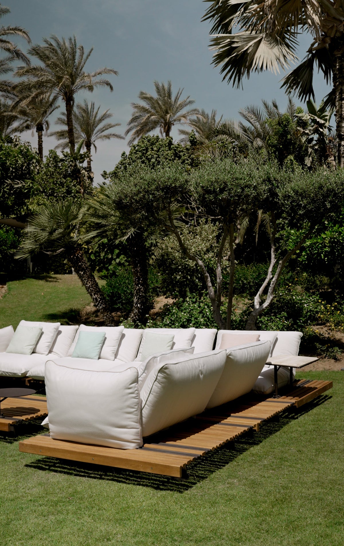 White Nest outdoor sectional sofa with piped cushions and a mixed-width teak platform in a garden setting.