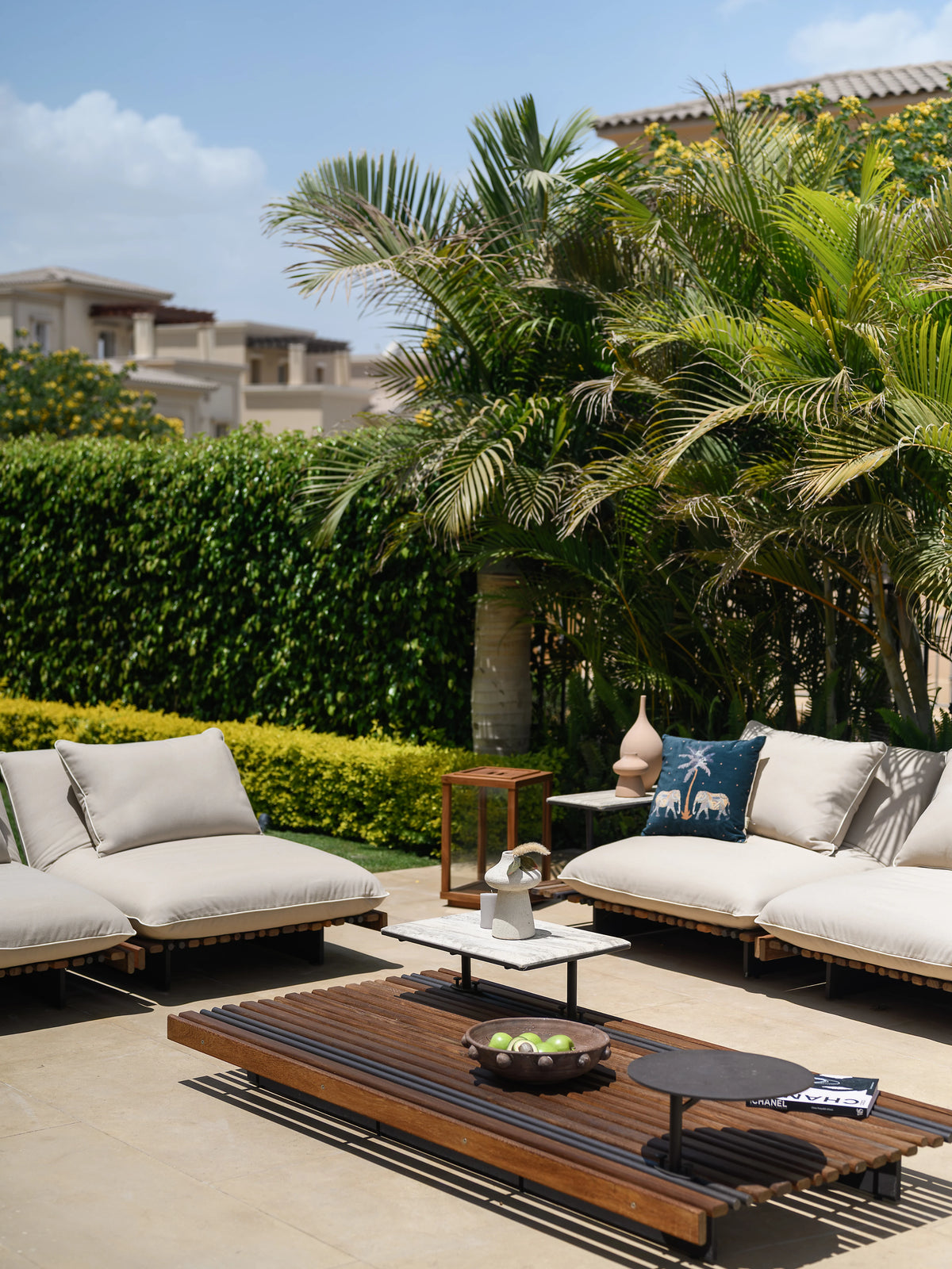 White Nest outdoor sofa arranged around a slatted teak Nest table with layered accent tables on a garden patio.