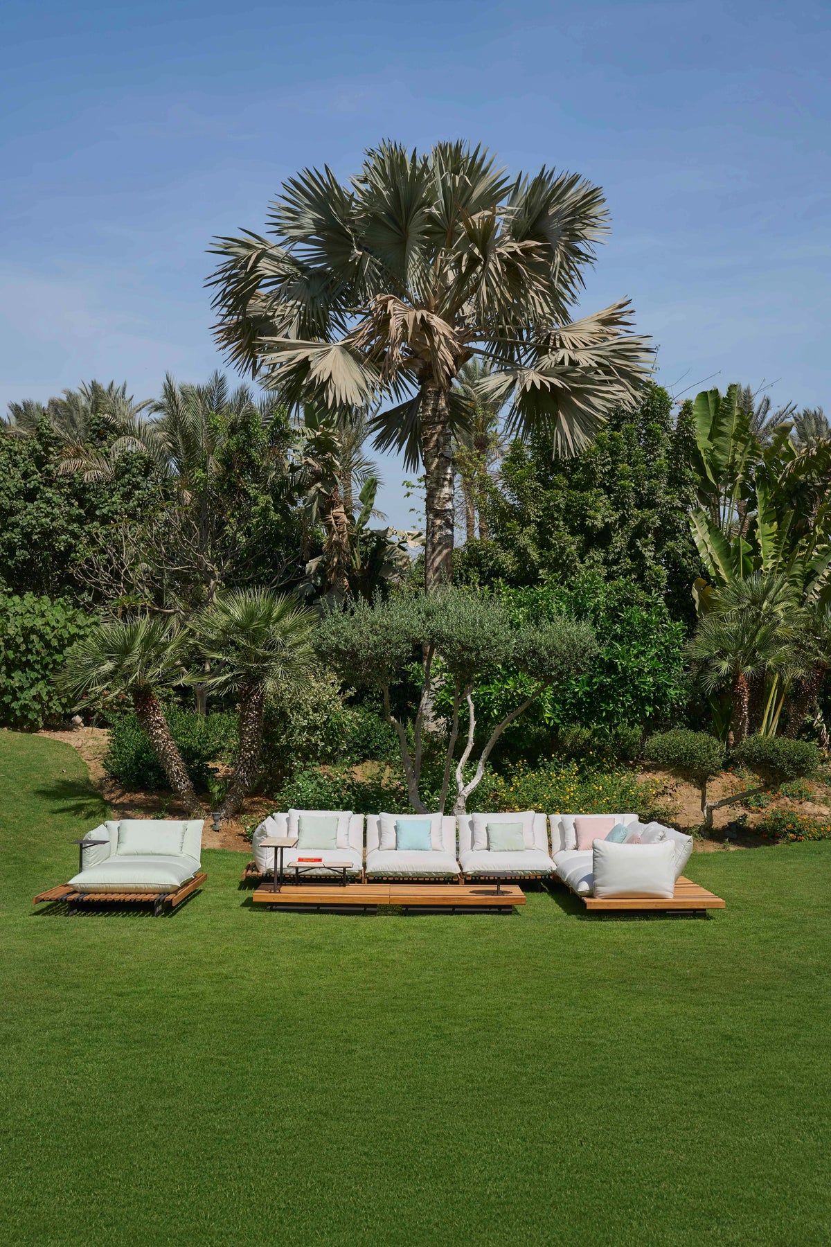 White Nest outdoor sofa with piped cushions, adjustable backrests, and a teak platform, arranged on a garden lawn.