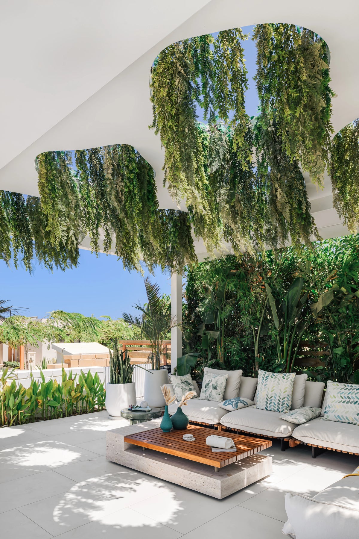 White Nest outdoor sofa paired with a slatted teak table and layered accent tables on a shaded garden patio.