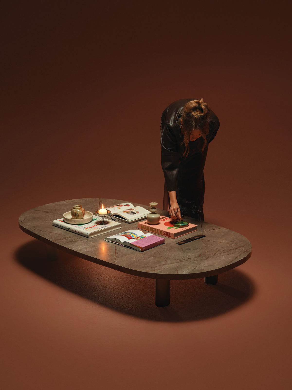 Woman arranging objects on the large Opal coffee table with a rounded brown marble laminate top and round steel legs.