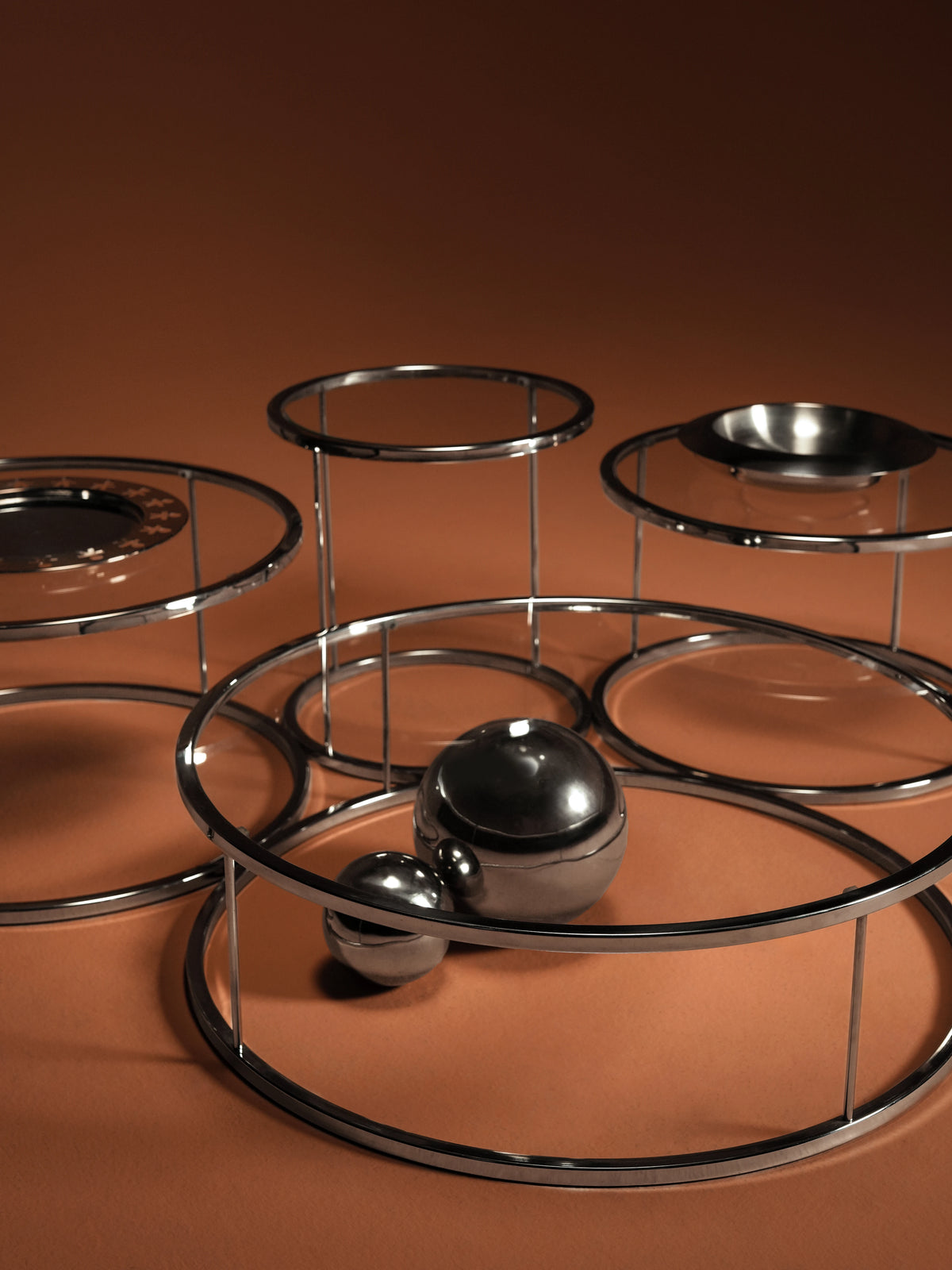 Close-up of the Orbit table collection, showing round transparent glass tops and stainless steel frames in varied heights and diameters.