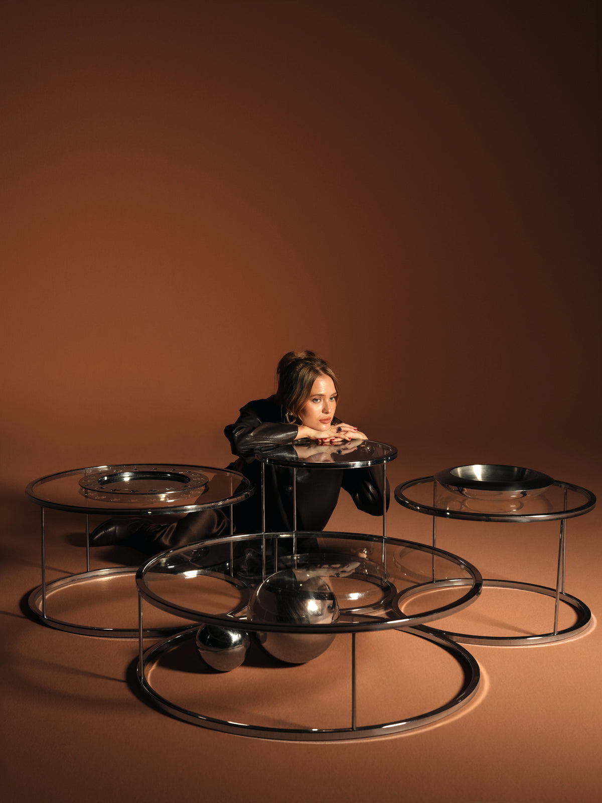 Woman seated behind a grouped arrangement of Orbit tables with round transparent glass tops and polished stainless steel frames.