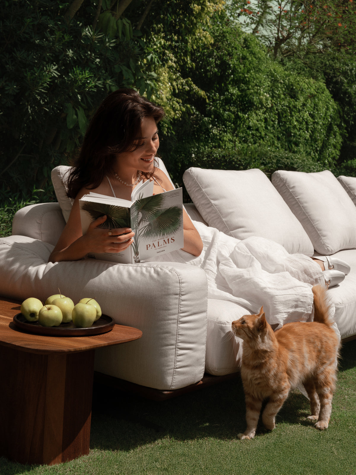 Outdoor Puff sofa in white upholstery, styled with he L-Corner teak side table and green garden backdrop.
