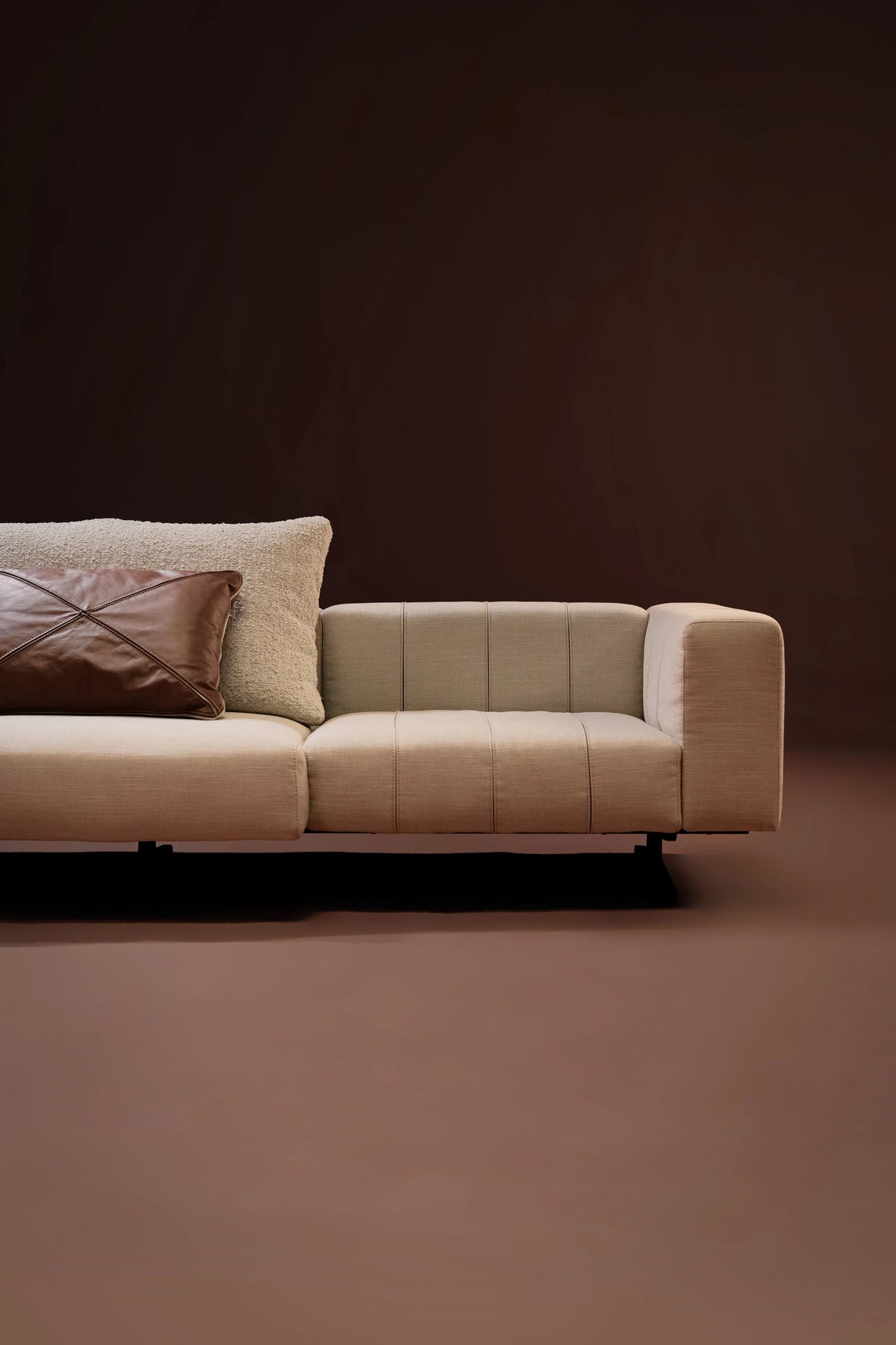 Elevation view of the Paella Sofa armrest with different seating designs and a textured back cushion layered with a leather throw pillow.
