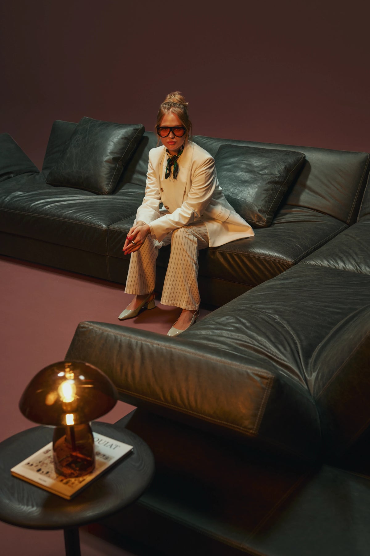 Woman seated on a black leather Panacea sectional sofa with adjustable backrests, angled armrests, and duck feather-filled cushions.