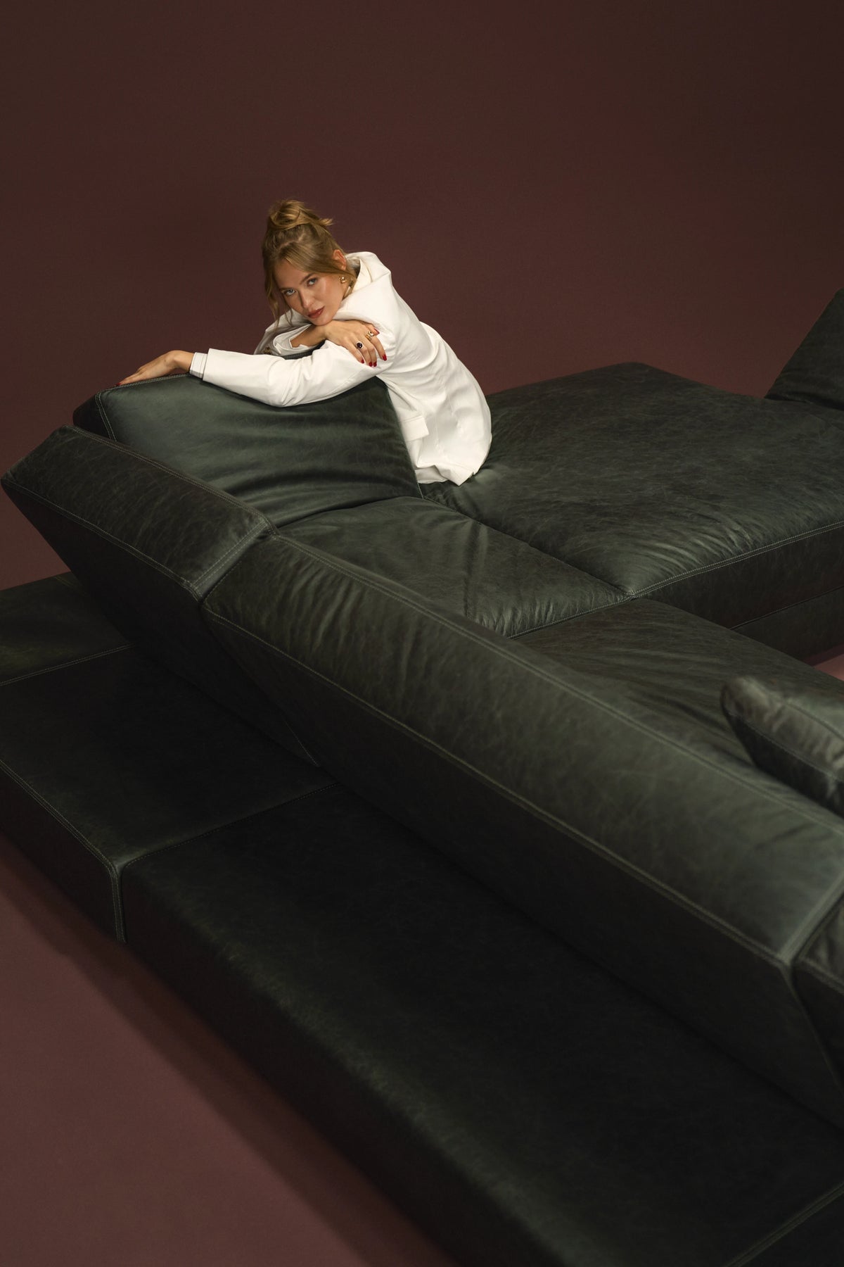 Woman leaning across the black leather Panacea sectional sofa with adjustable backrests and armrests opened into a low layout.