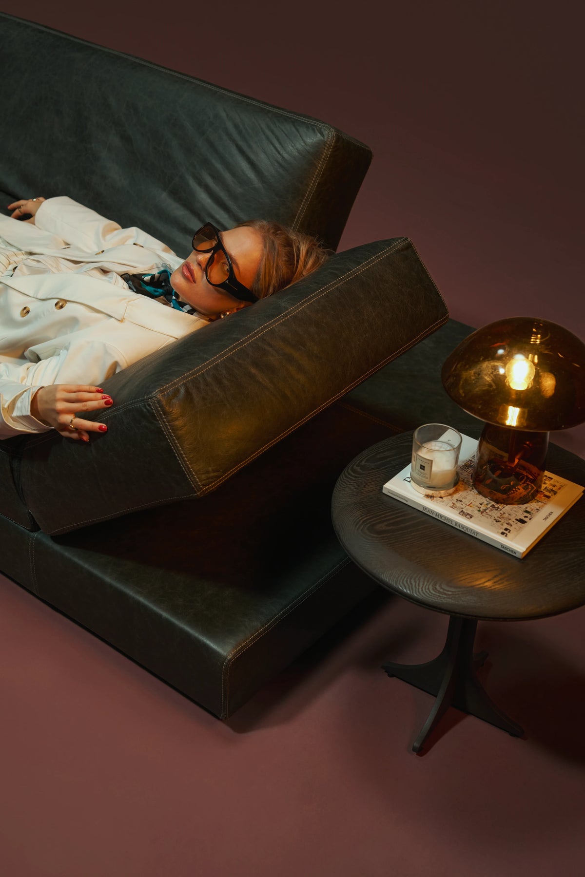 Woman reclining on a black leather Panacea sofa with the adjustable armrest raised for support.