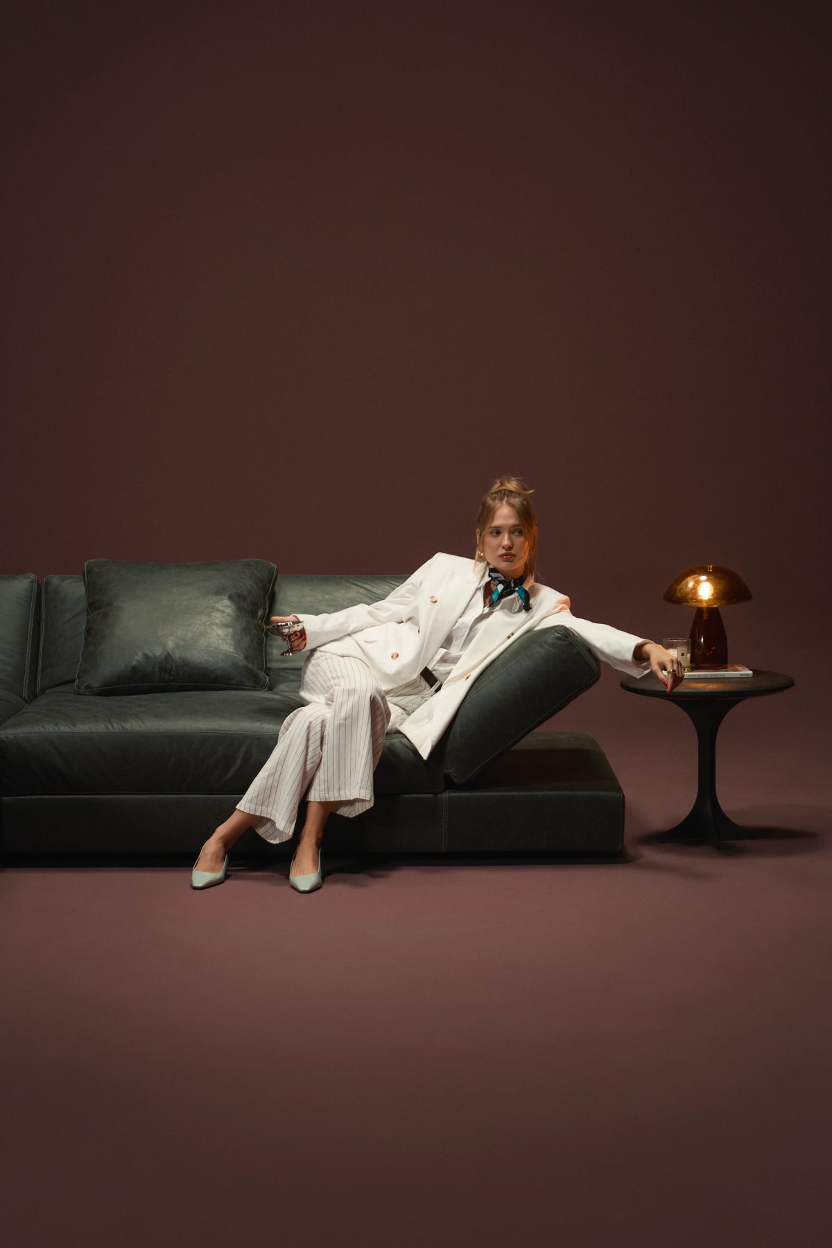 Woman seated on a black leather Panacea sofa beside its raised adjustable armrest.