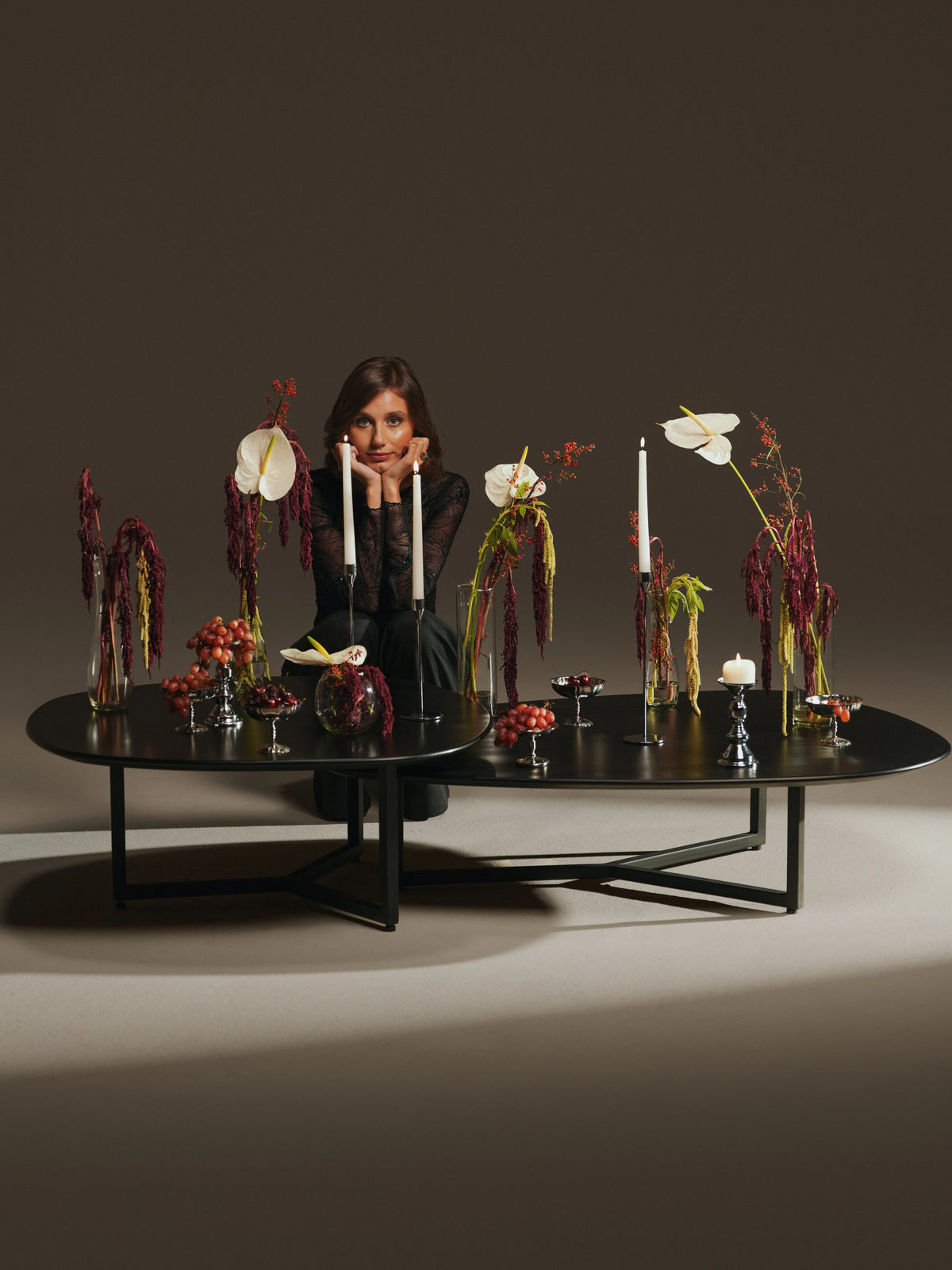 Woman seated behind a pair of black Pebble tables with asymmetrical painted plywood tops and slim steel legs.