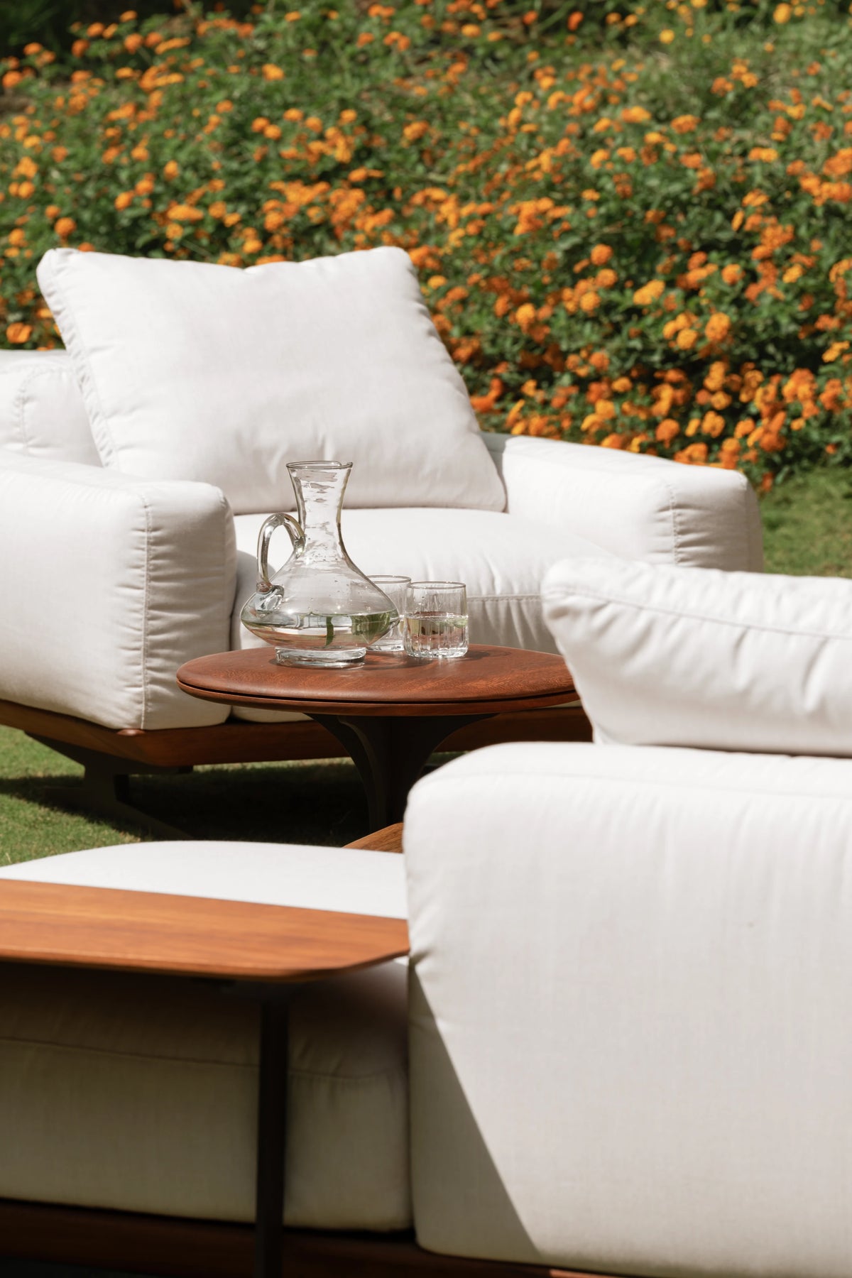 White Puff outdoor seating arranged around a small round Glide table with a teak top and dark metal pedestal base.
