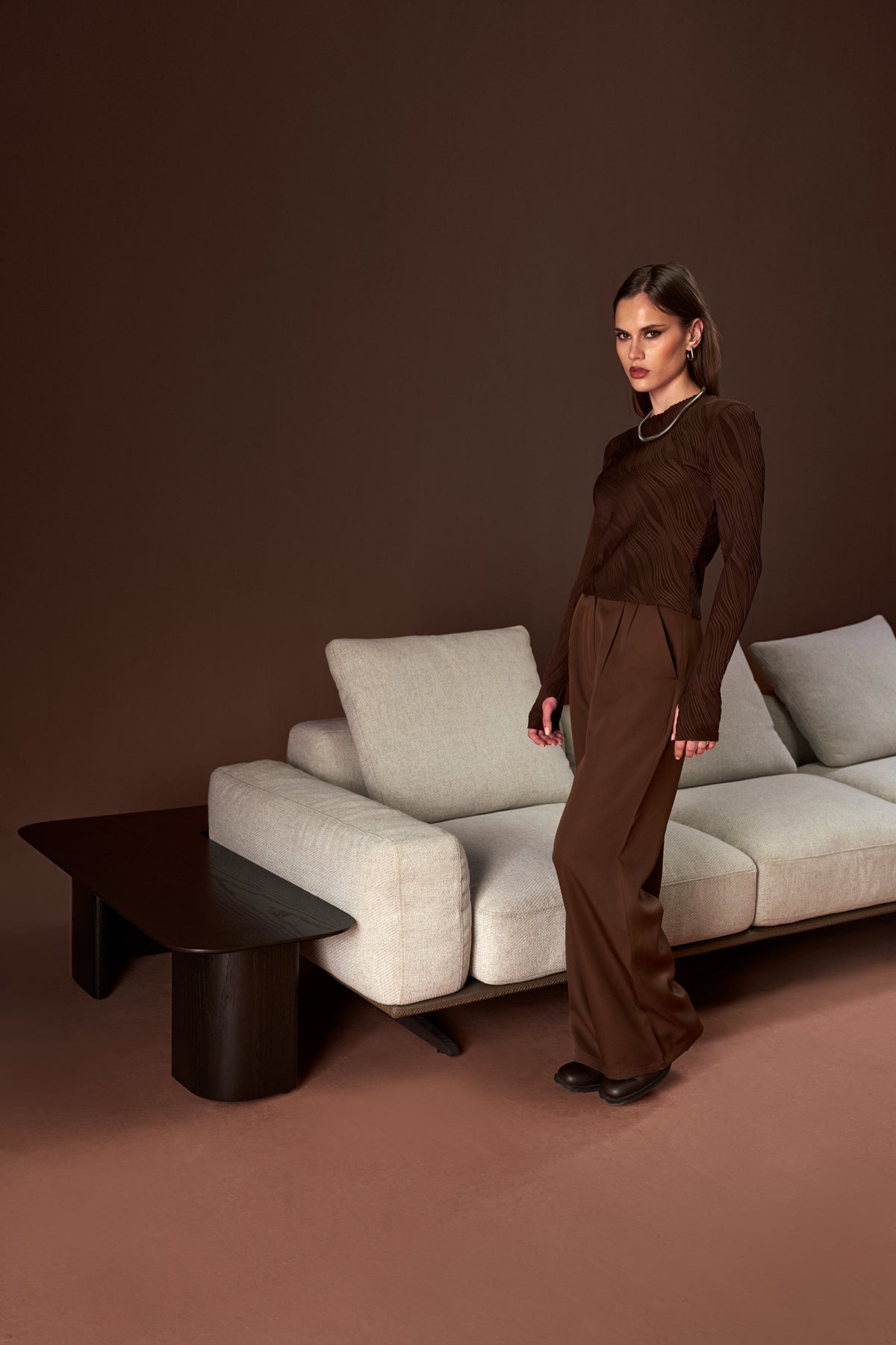Model standing beside the Puff sofa with its low back, cushioned arms, and leather-wrapped platform detail.