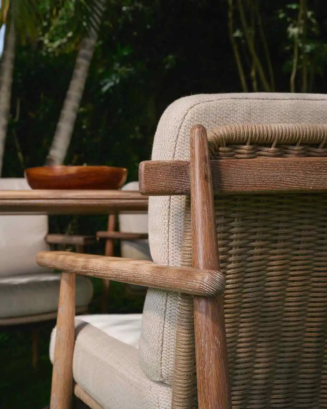 Close view of the Retro outdoor armchair showing its solid wood frame, rounded armrest, woven rope backrest and beige cushions.