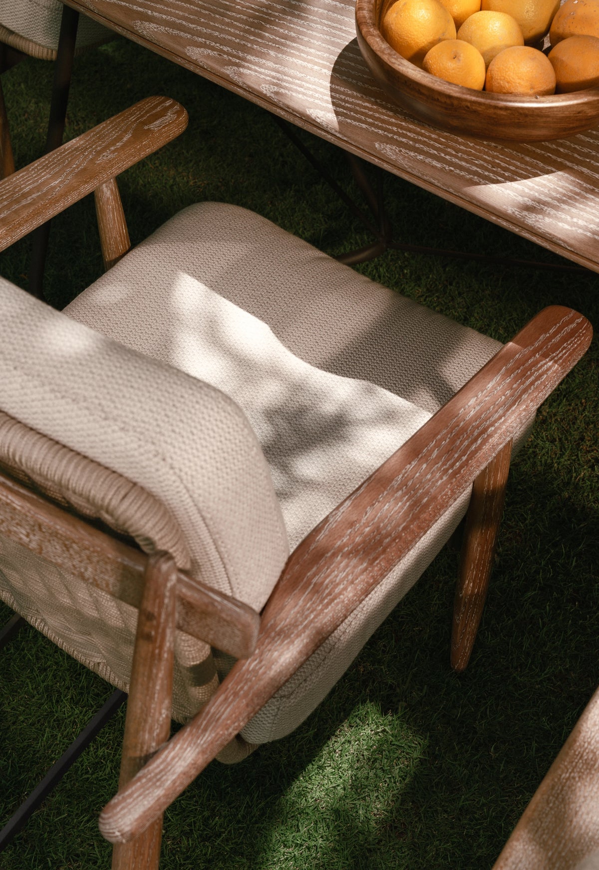Close-up of Retro dining chair showing solid wood armrest and frame with cream upholstered seat, styled outdoors beside Retro dining table.