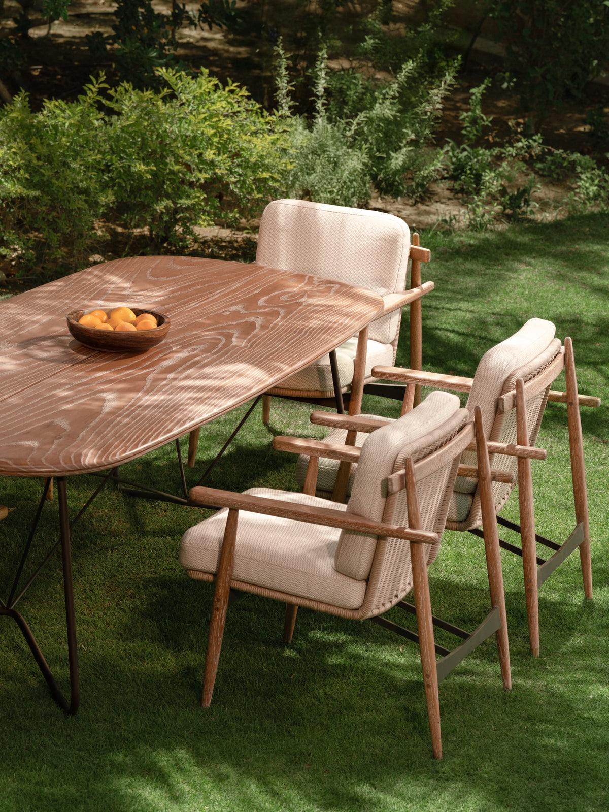 Side view of Retro dining table with solid wood top and cushioned Retro chairs in solid wood and electrostatic-coated stainless steel, styled in a garden setting.
