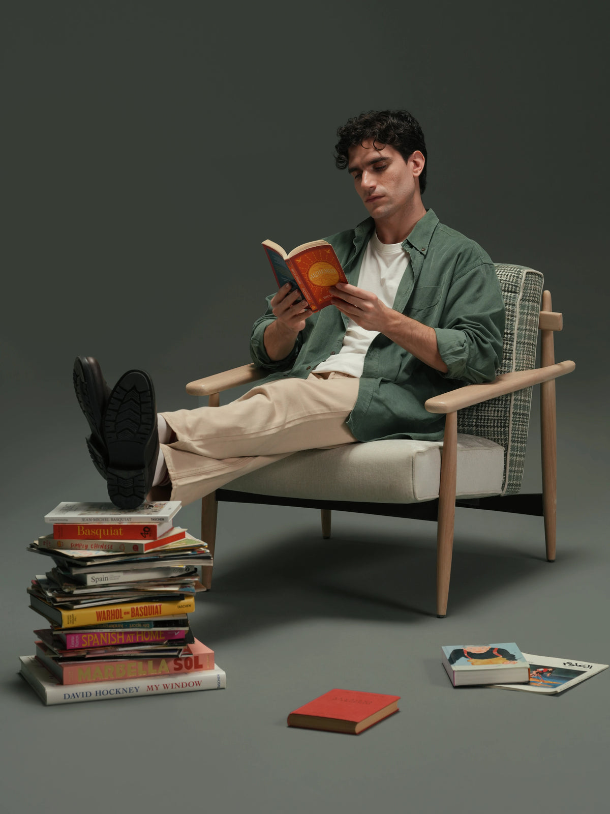 Man reading in the Retro Lounge armchair, featuring a solid wood frame, plaid backrest, light upholstered seat, and curved rectangular armrests.