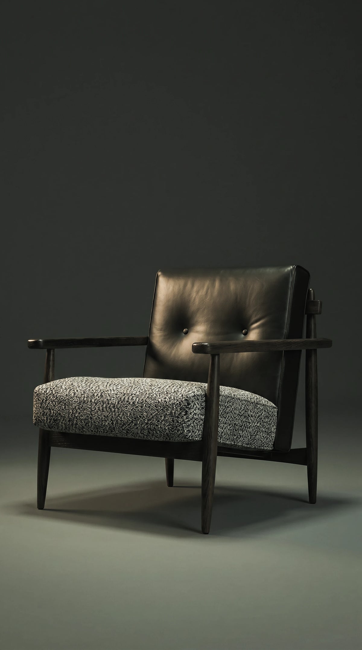 Angled front view of the Retro Lounge armchair with a black leather capitonné backrest, textured grey seat cushion, and dark solid wood frame.