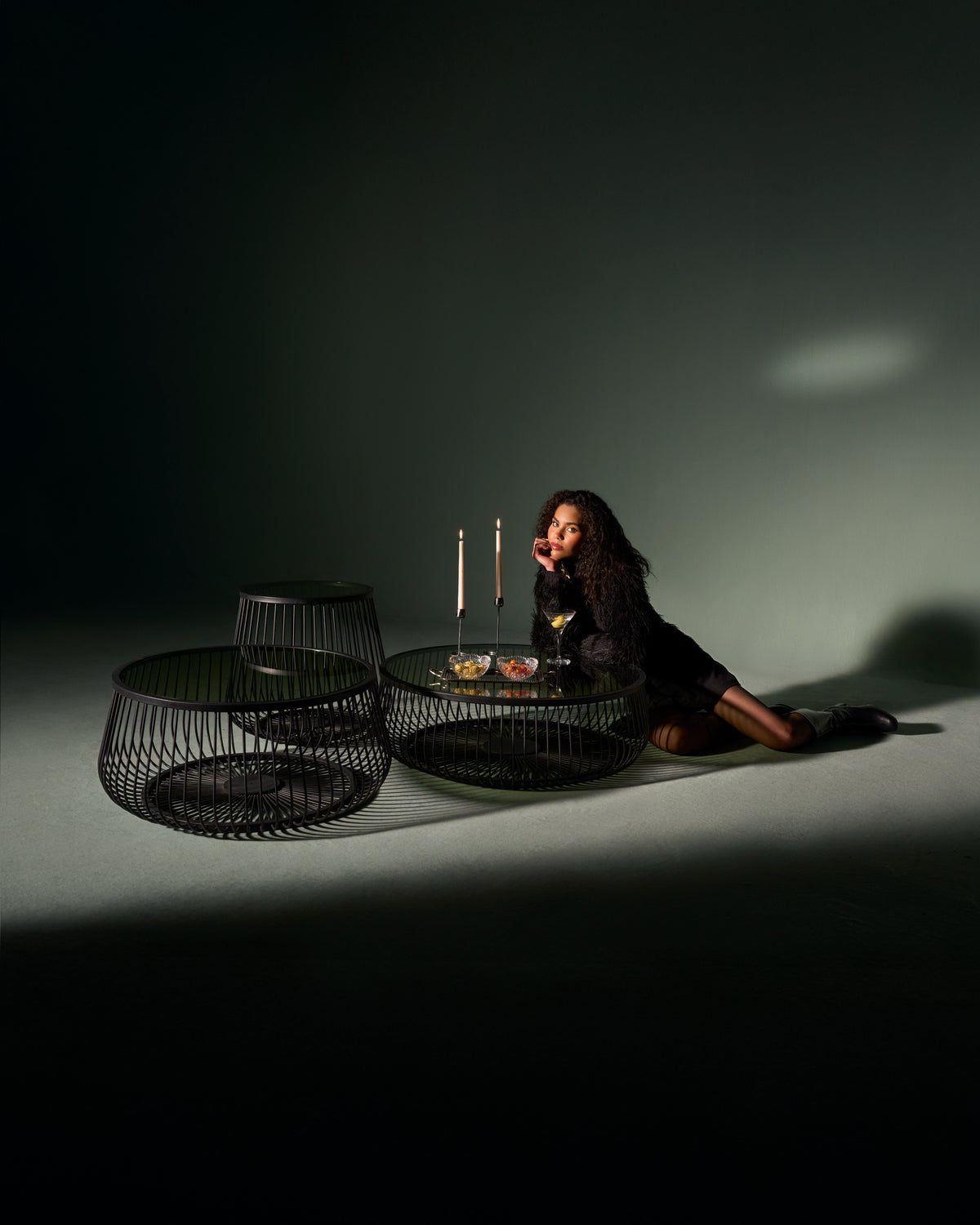 Model leaning near Ring tables with open black metal bases and glass tops, highlighting their circular design.