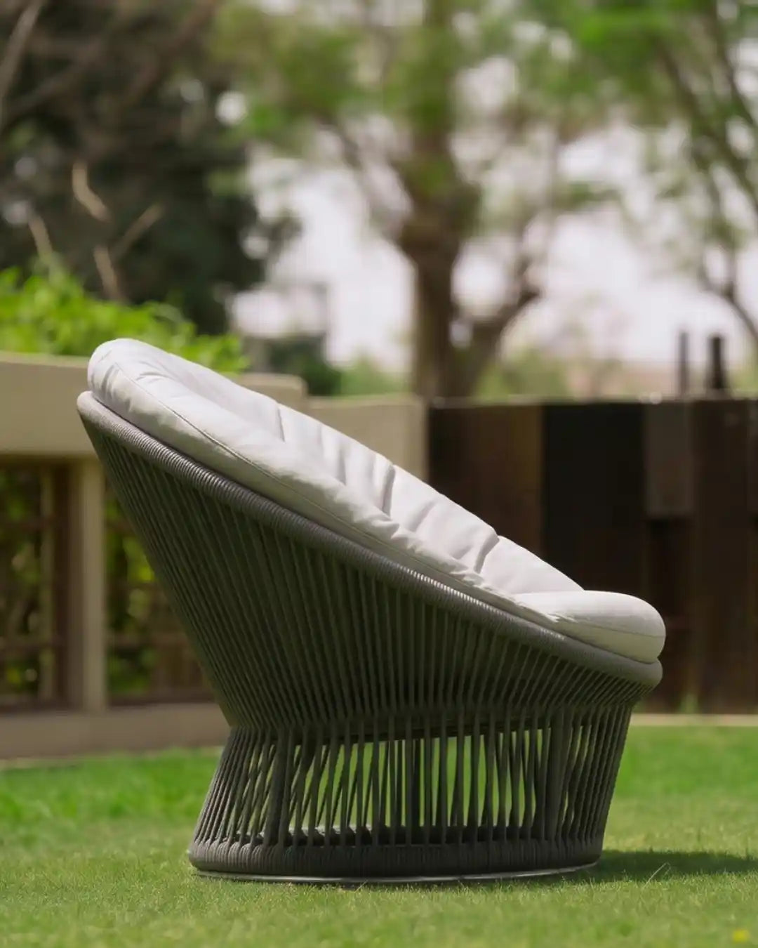Side view of the Sun outdoor armchair showing its low circular profile, dark grey handwoven rope frame and light cushion.