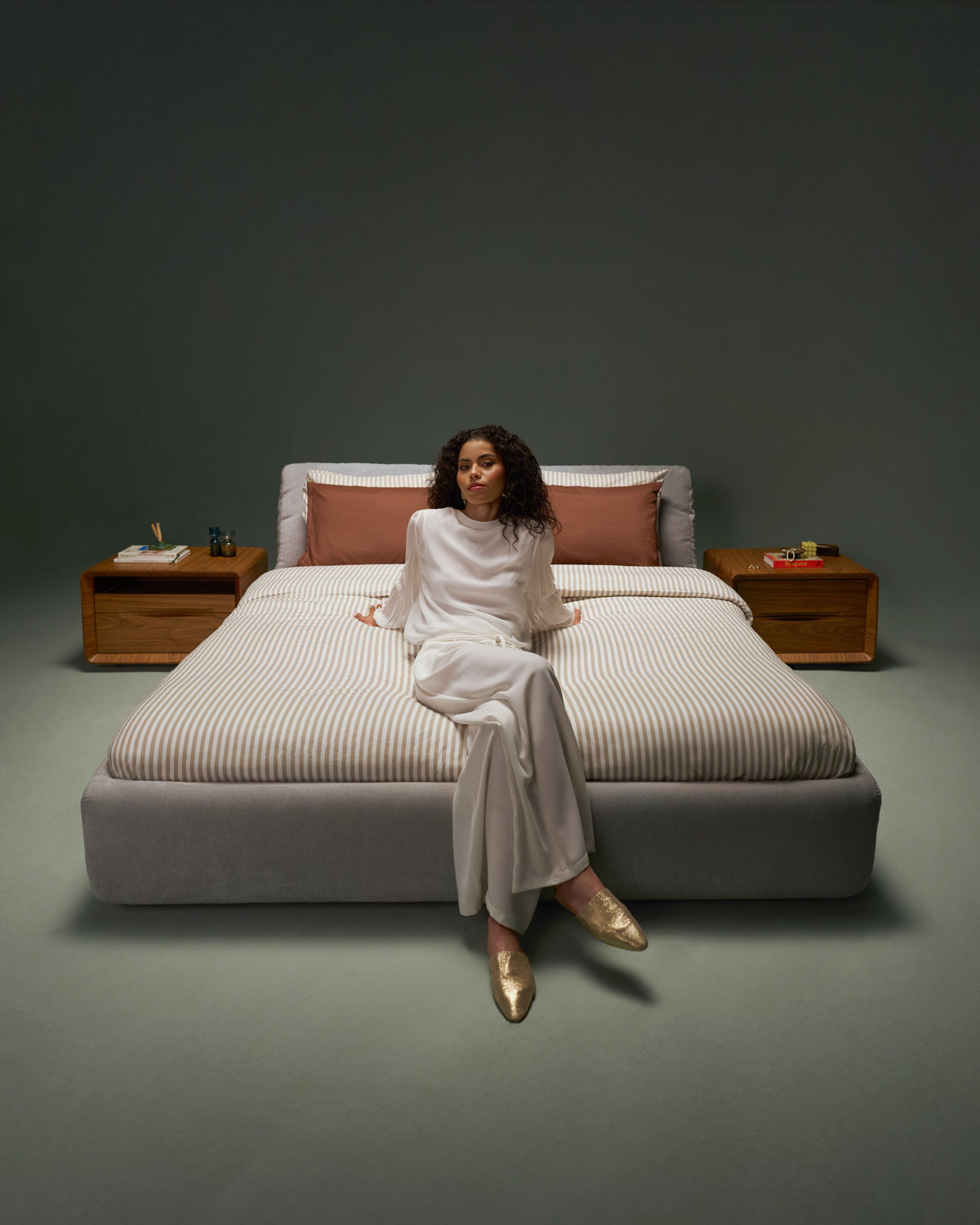 Model seated on Snug Bed in light grey upholstery with recessed mattress and tilt-adjustable backrest.