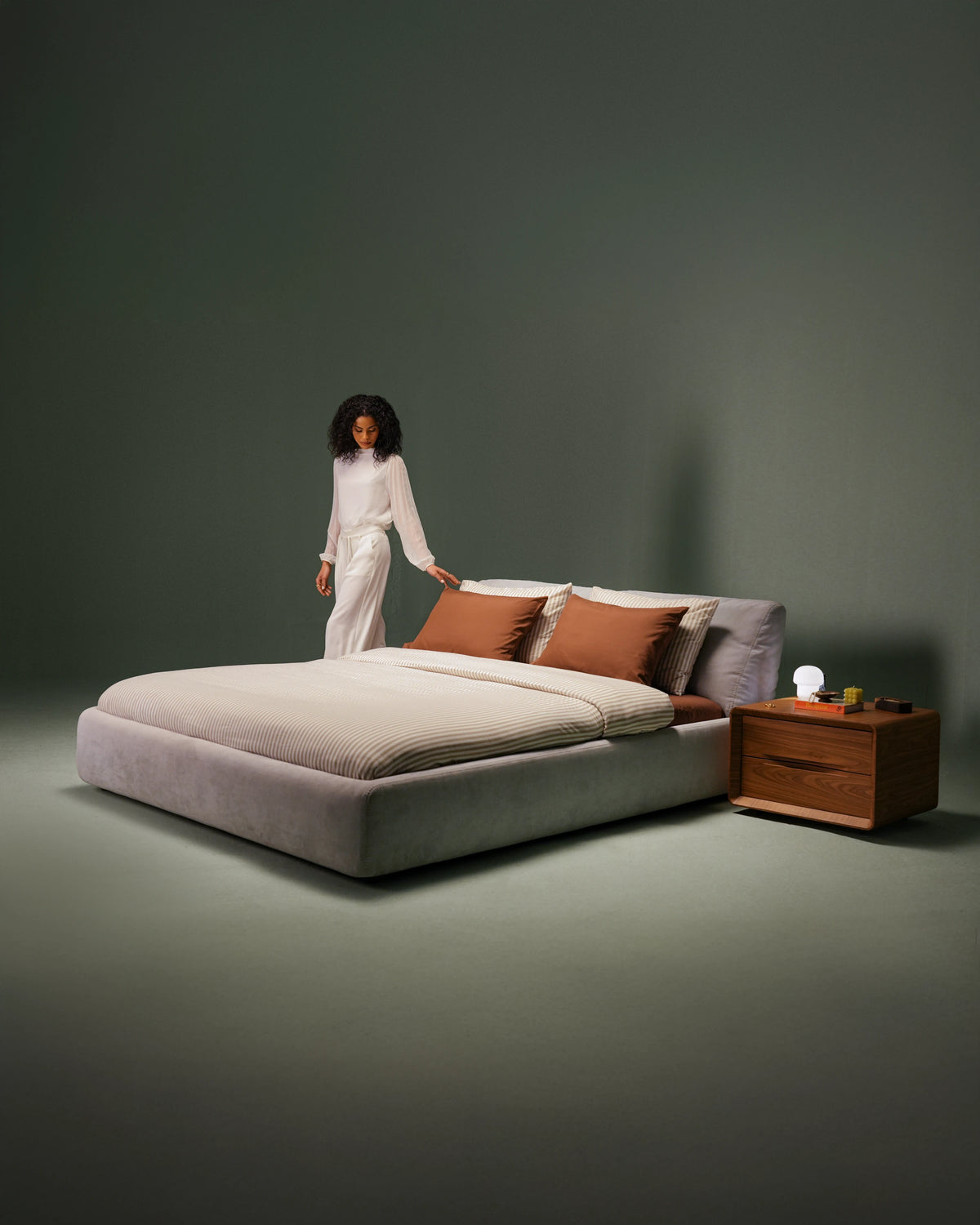 Snug upholstered bed with independently adjustable backrests, striped bedding and a wooden Groove two-drawer nightstand in a dark green setting.