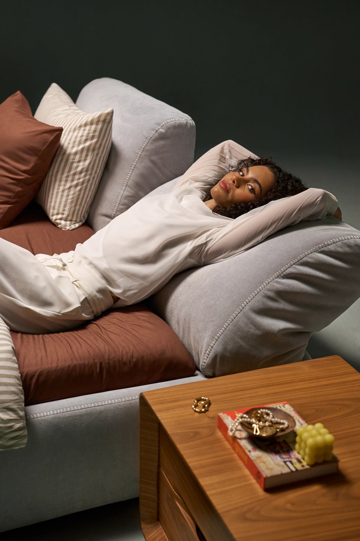 Woman lying against one reclined backrest of the Snug bed beside a wooden nightstand, showing its independent adjustment mechanism.