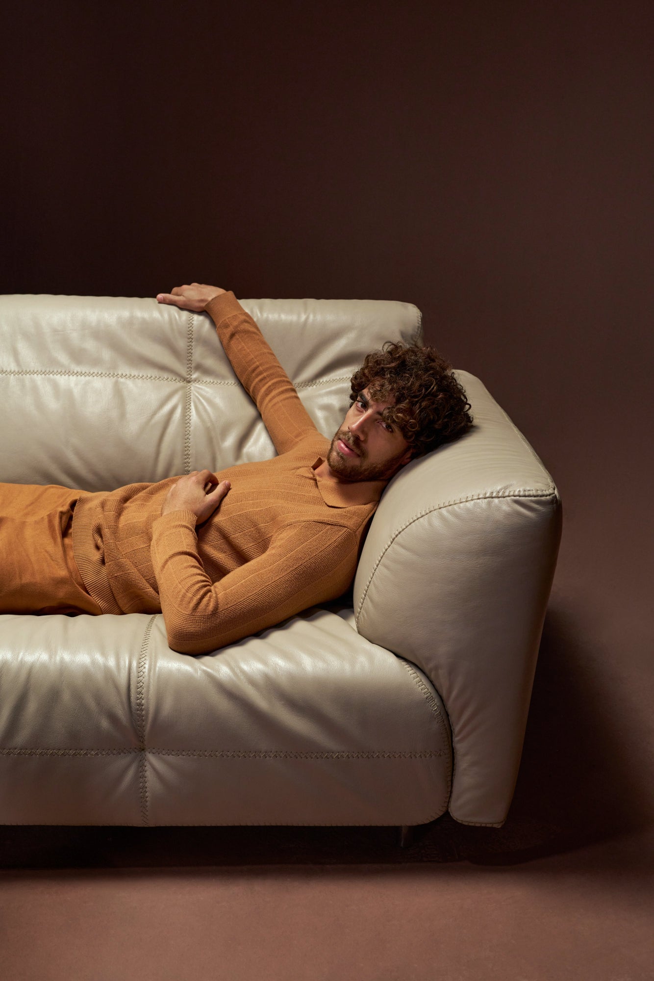 Model reclining on the Snug sofa in beige genuine leather with stitched upholstery and wide reverse P-arm design.