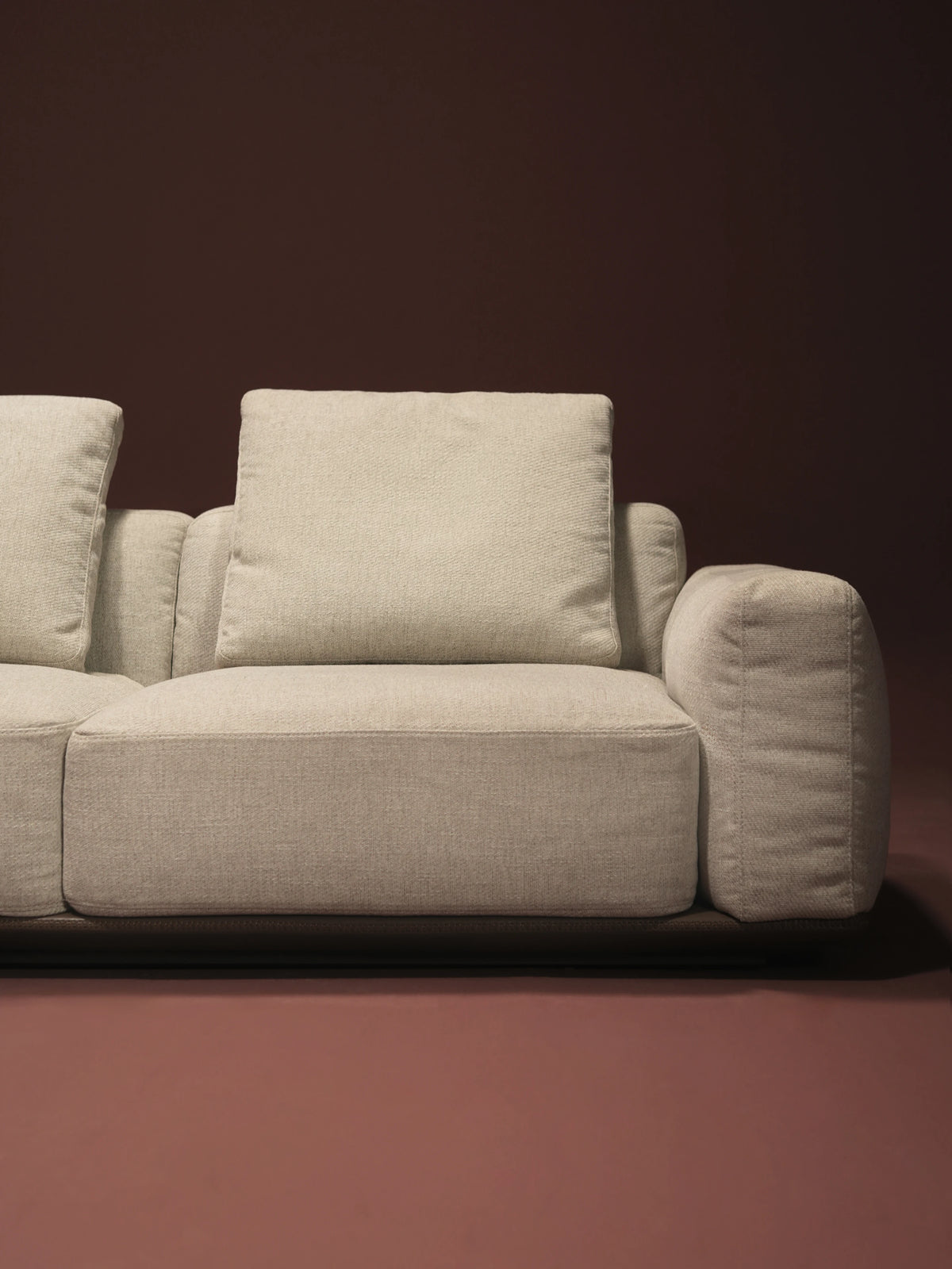 Close-up of the beige Soffio sofa showing its tall seat cushion, loose back cushion, padded armrest, and leather platform.