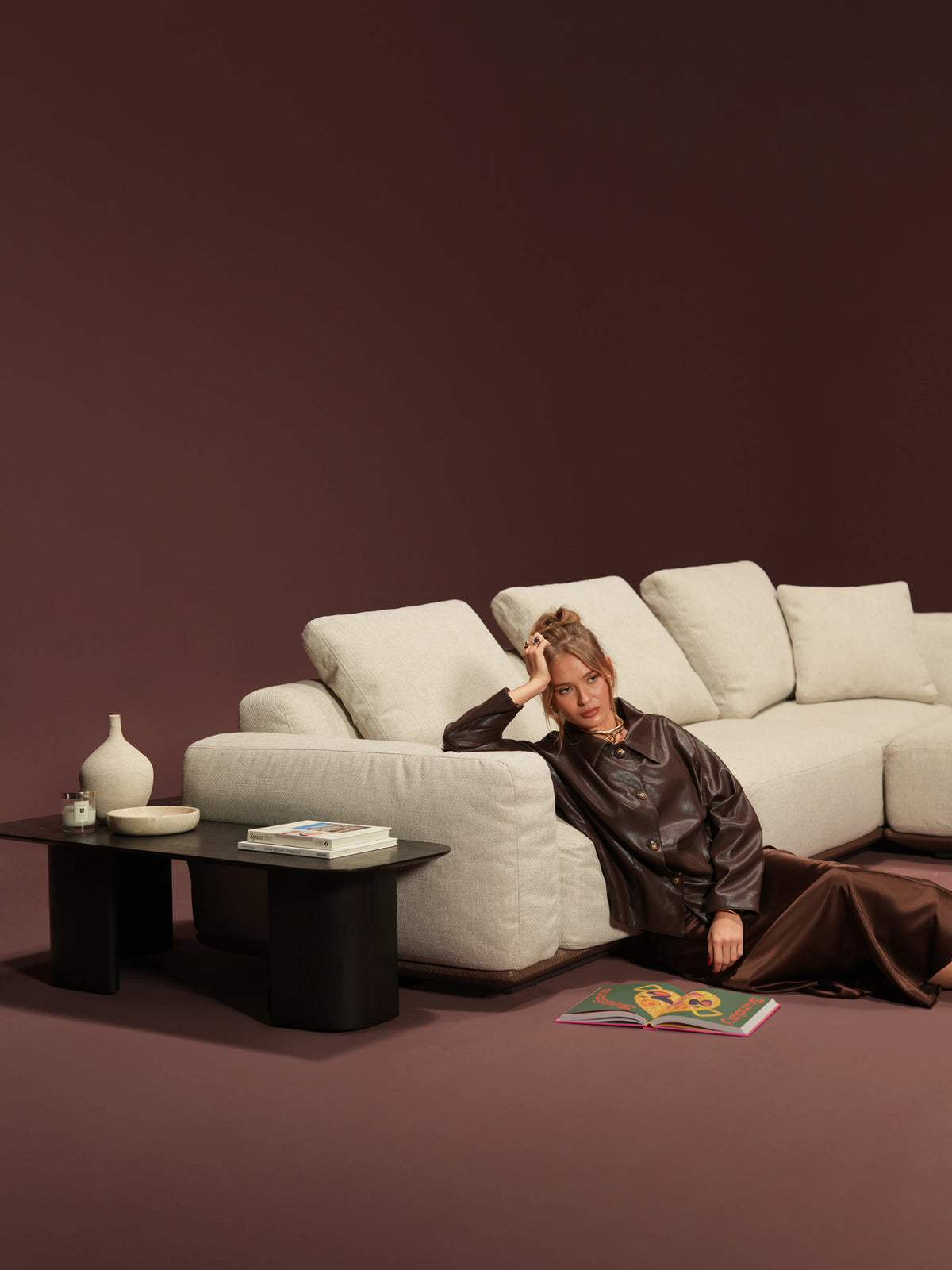 Woman leaning against the broad upholstered armrest of a beige Soffio sofa with deep seating and loose back cushions.