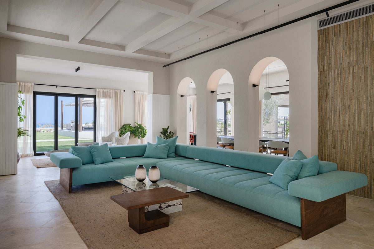 Angled view of the blue Sol sectional sofa, showing its spacious modular layout, stitched seat cushions, and exposed solid wood frame.
