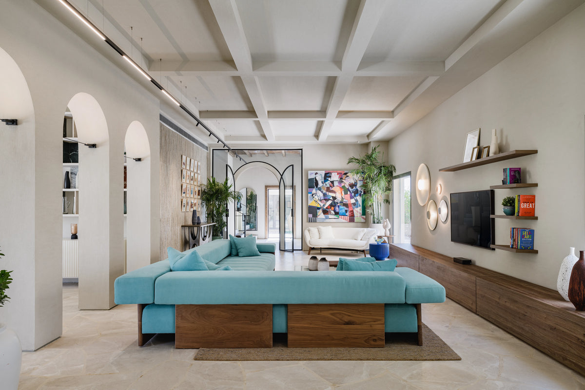 Rear view of the blue Sol modular sofa, highlighting its open profile, exposed solid wood panels, and integrated low table armrest.