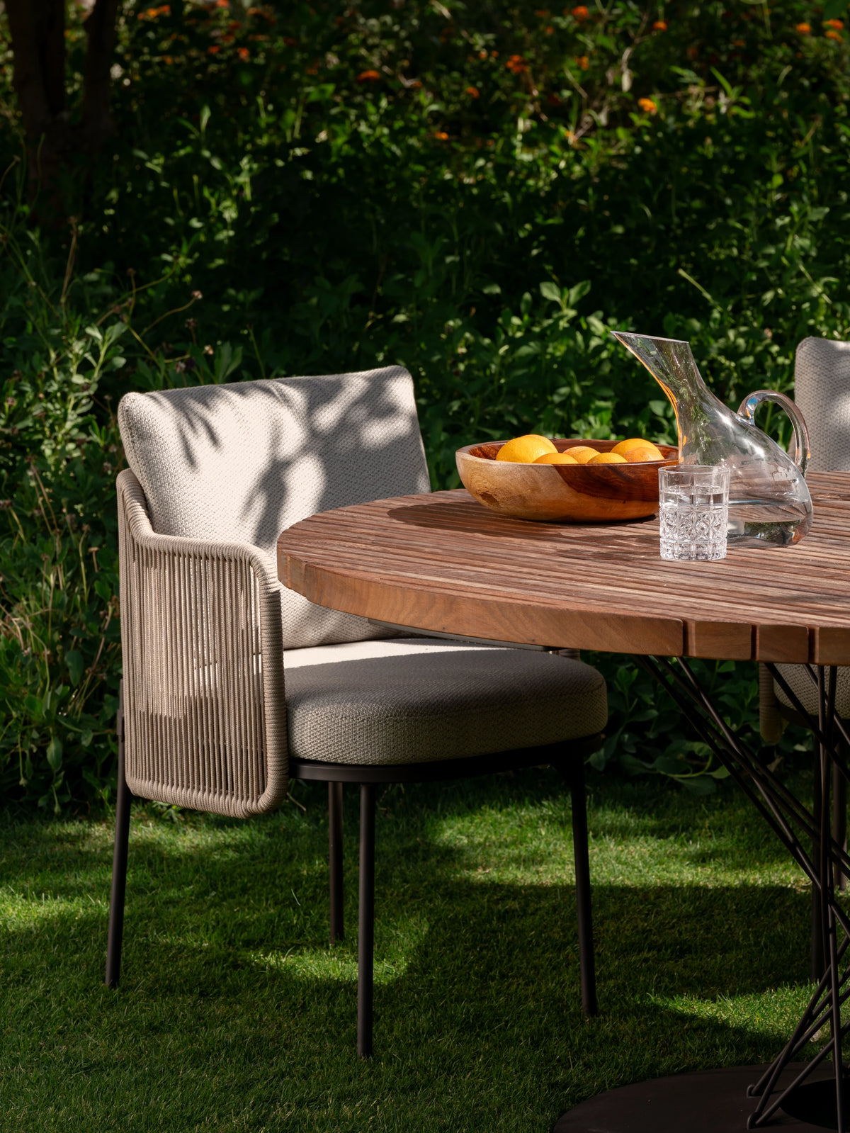 Side view of Cord dining chairs with woven rope backrest and upholstered cushion, paired with Spiral teak dining table.