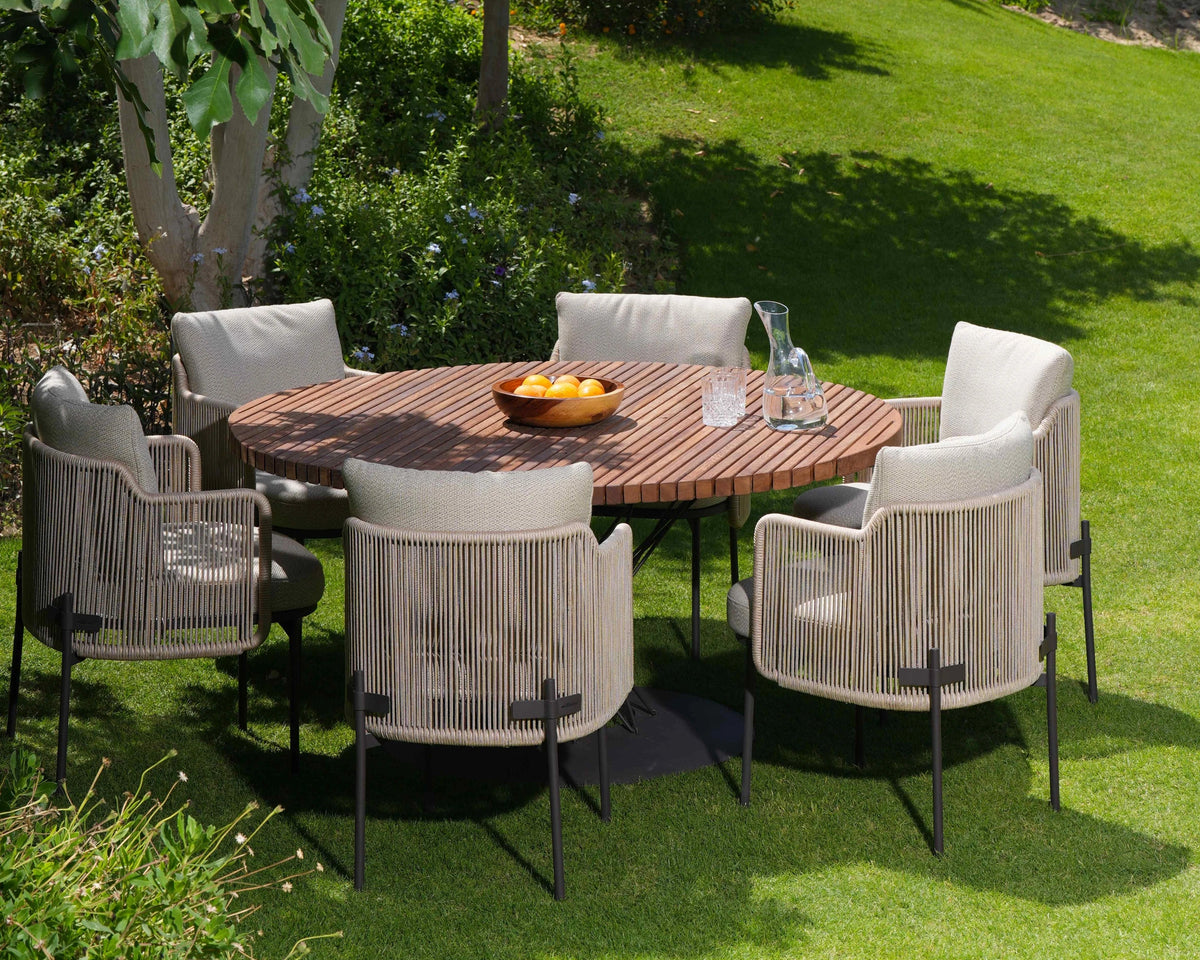 Round Spiral outdoor dining table with a solid teak slatted top and stainless steel rod base, surrounded by six beige rope Cord dining chairs.