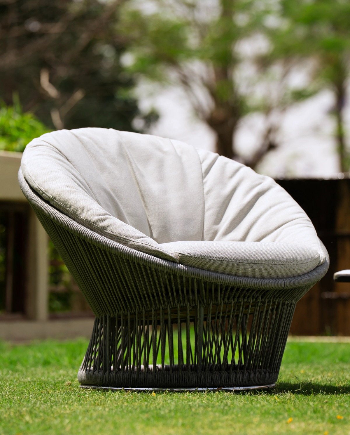 Sun outdoor armchair with a circular dark grey handwoven rope frame and light cushioned interior, photographed on a garden lawn.