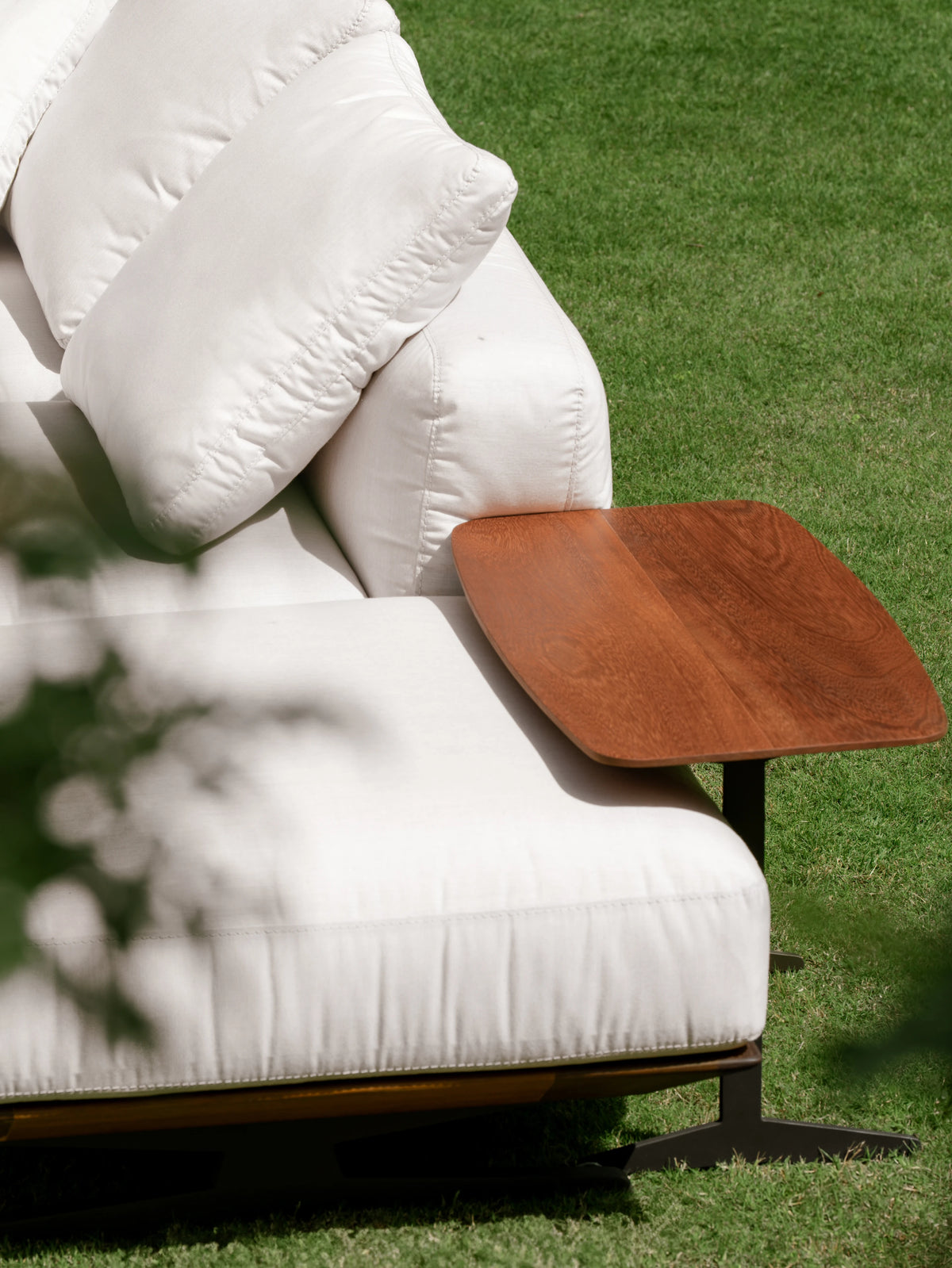 Teak Topper table positioned over the white seat cushion of the Puff outdoor sofa, supported by slim dark metal legs.