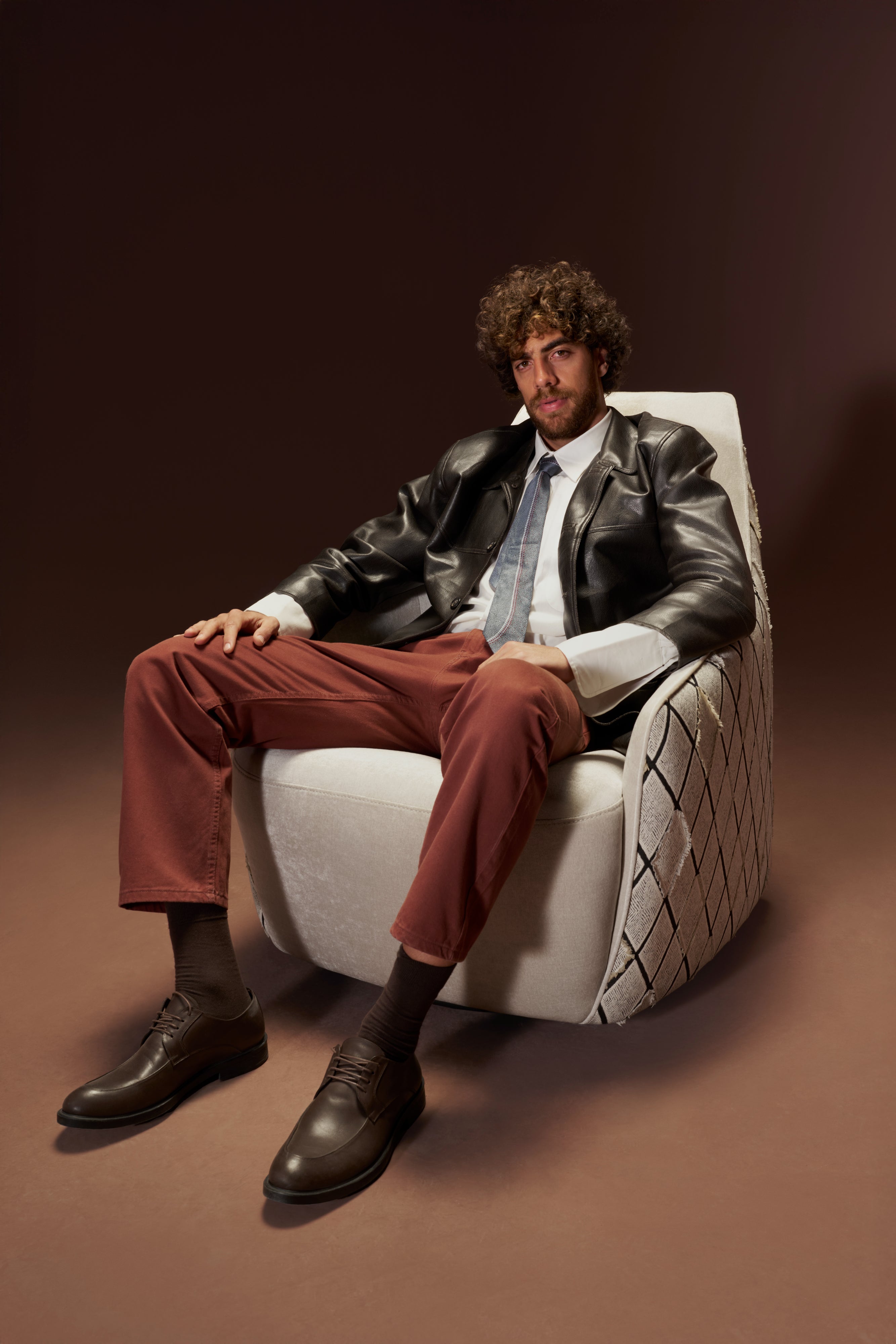 Model seated in the Windsor High Armchair with tall backrest and stitched diamond-patterned sides in beige fabric.