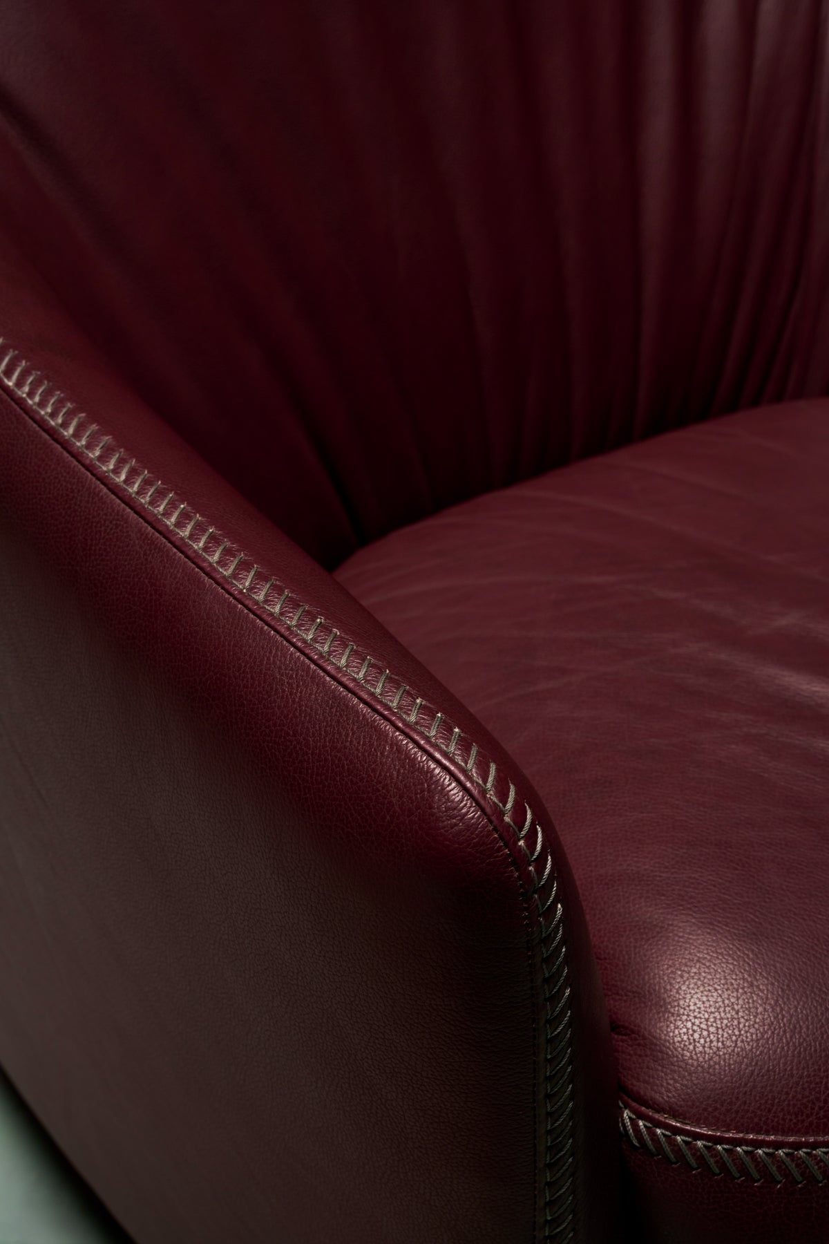 Close-up of Windsor Low armchair in burgundy leather showing overcast stitching along the armrest and seat cushion edge.