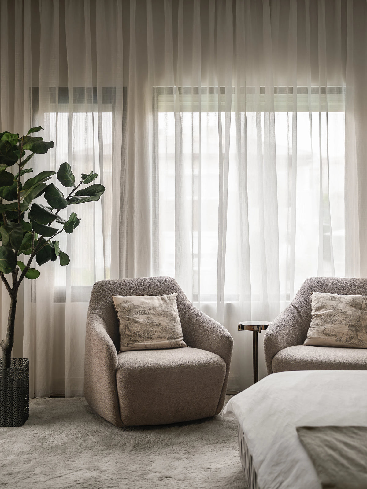 Pair of beige fabric Windsor Low armchairs with piping detail and patterned cushions, positioned beside a bedroom window.
